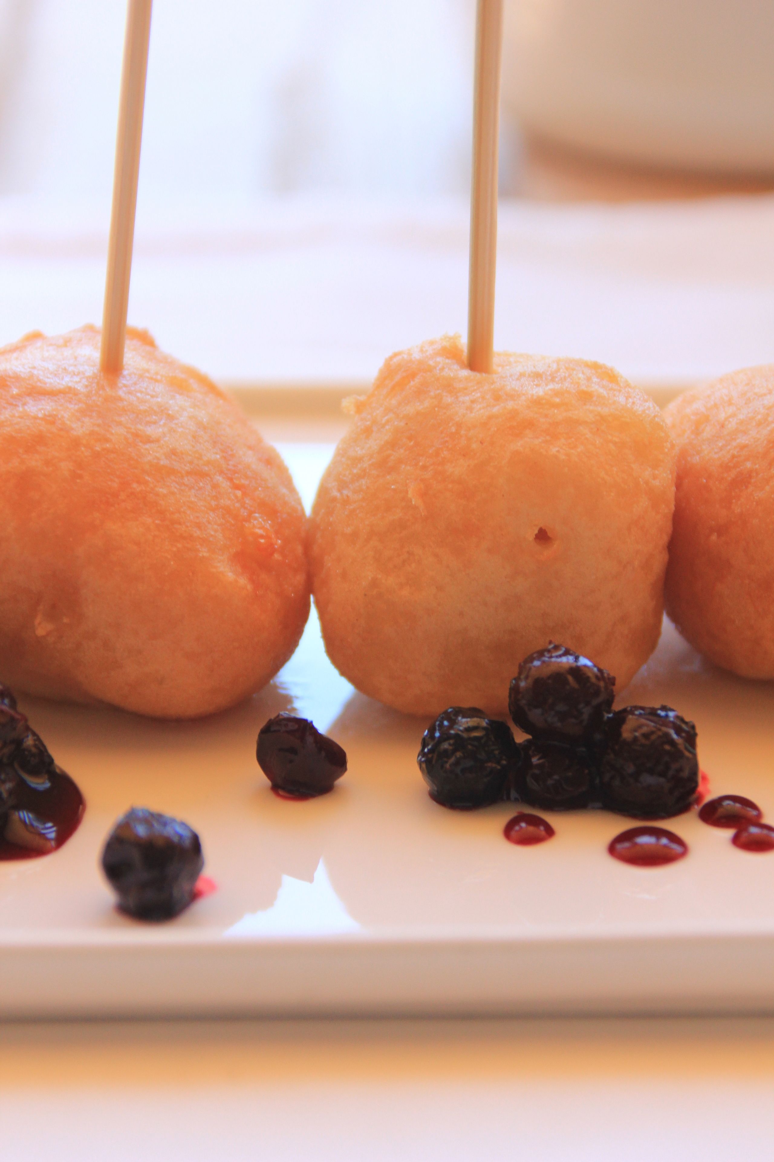 A plate with three corn dogs on sticks and some berries.