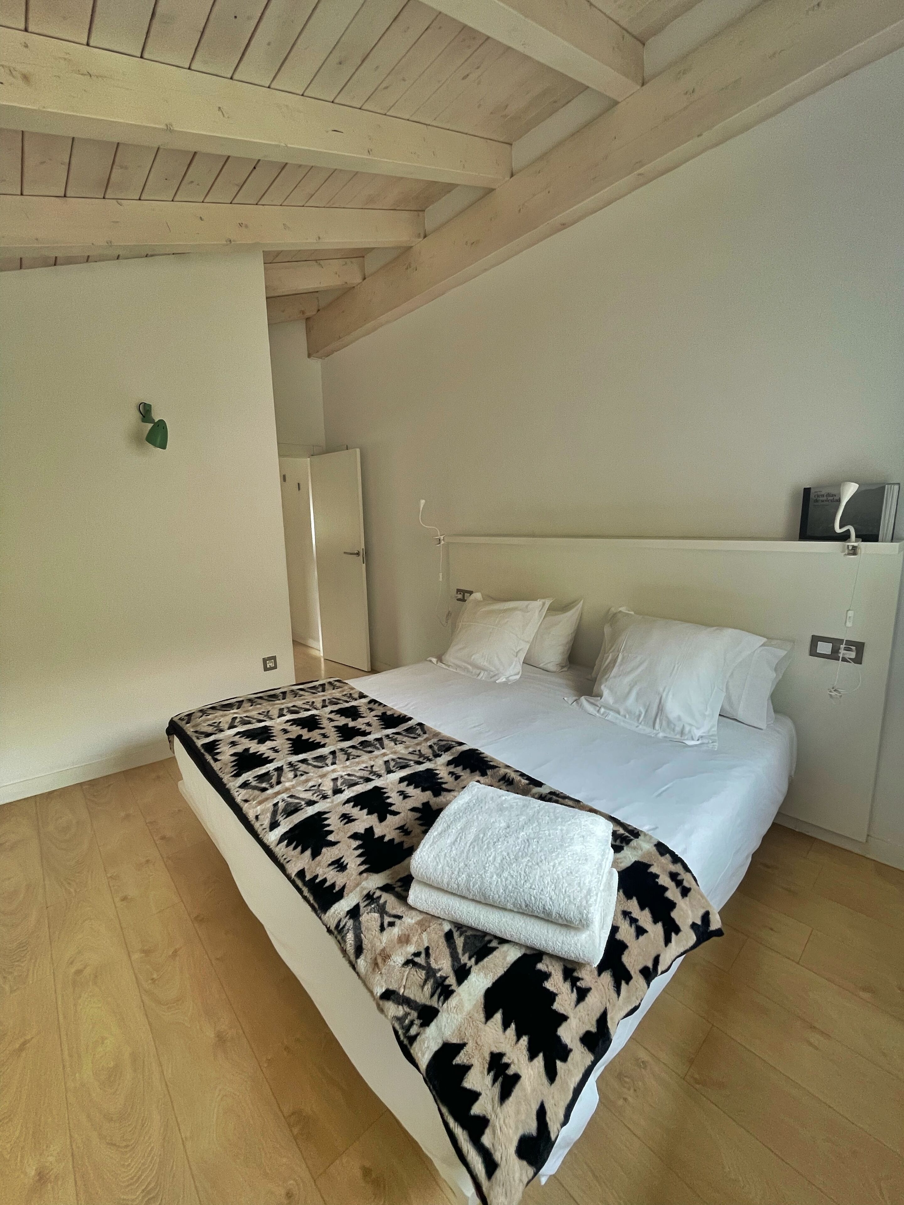Un dormitorio con cama, techo de madera y pared blanca.