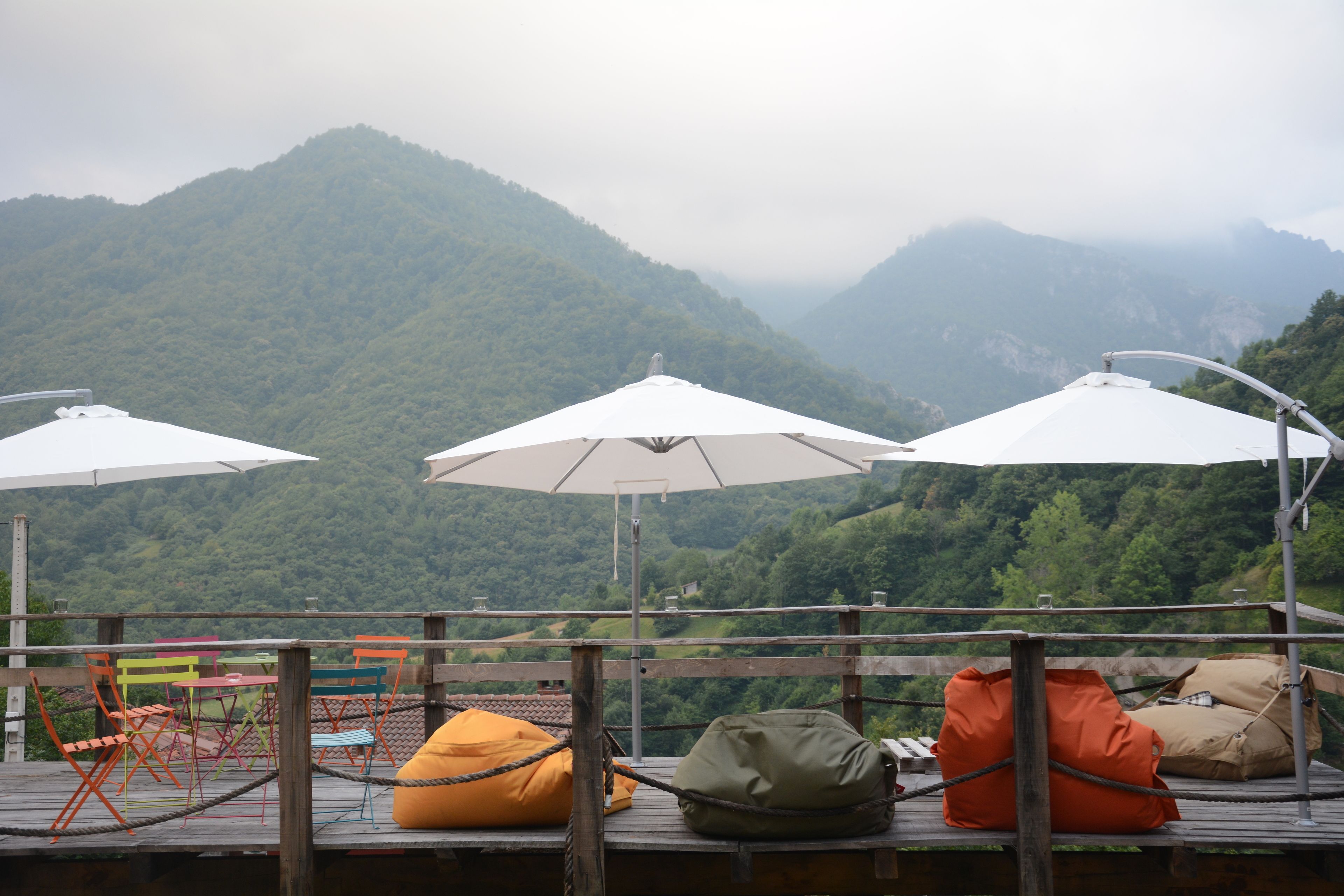 Une terrasse en bois avec des sièges d’extérieur, comprenant des chaises colorées et des fauteuils en forme de sac, offrant une vue sur un paysage montagneux.