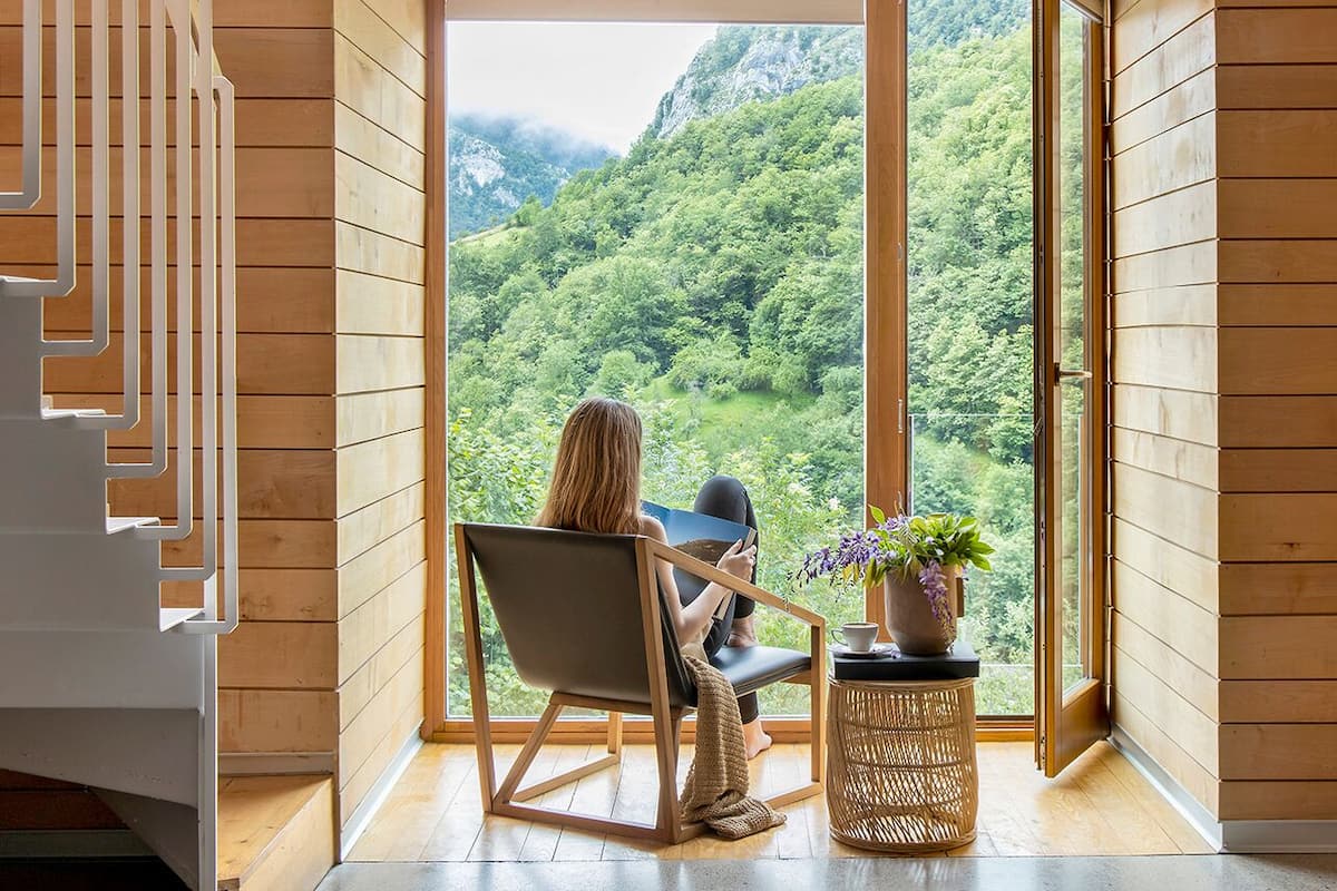 A room with a large window offering a view of a forested mountain.