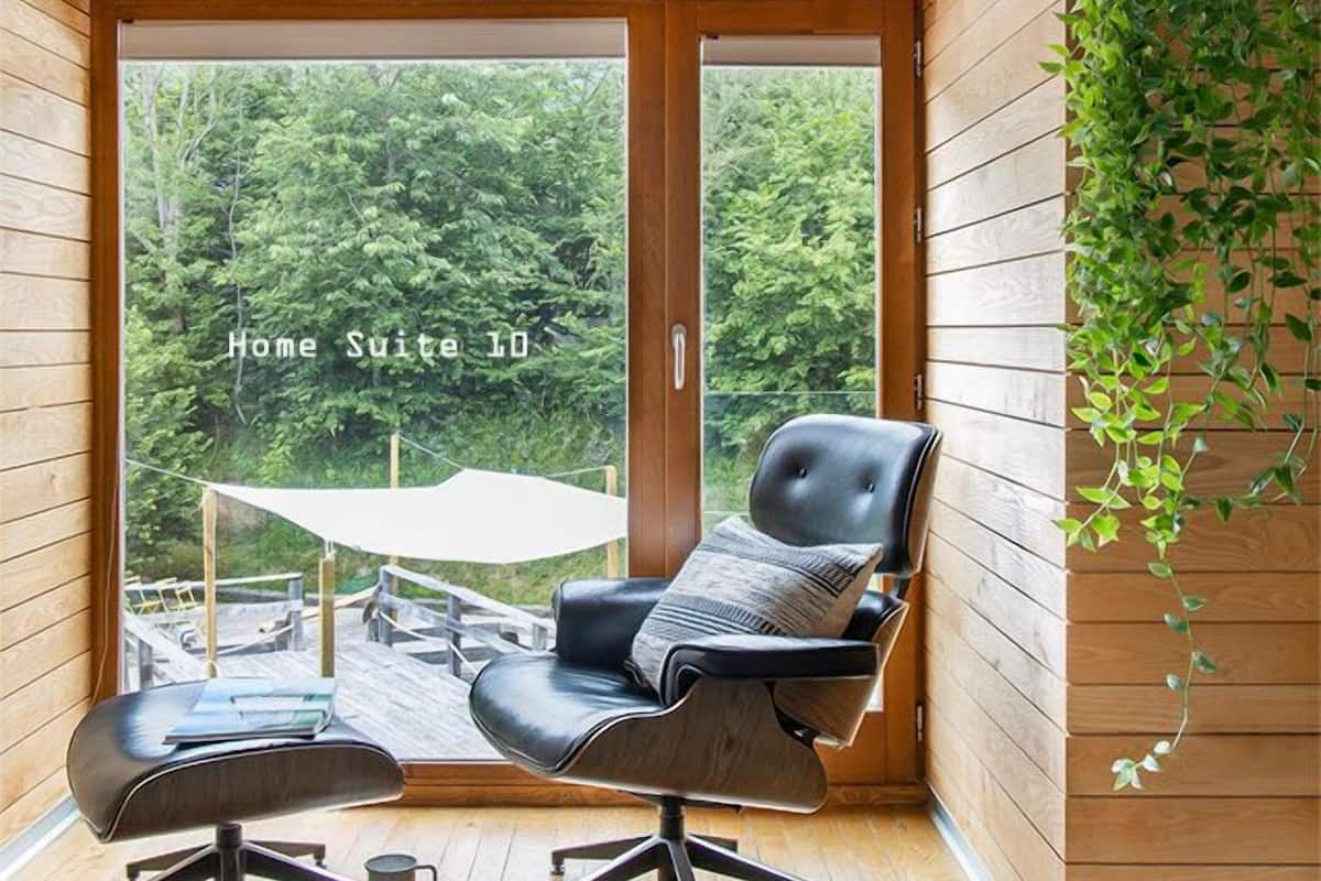 A modern home suite with a large sliding glass door leading to an outdoor deck, a black leather chair, a small table, and a hanging plant.