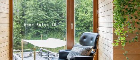 A modern home suite with a large sliding glass door leading to an outdoor deck, a black leather chair, a small table, and a hanging plant.