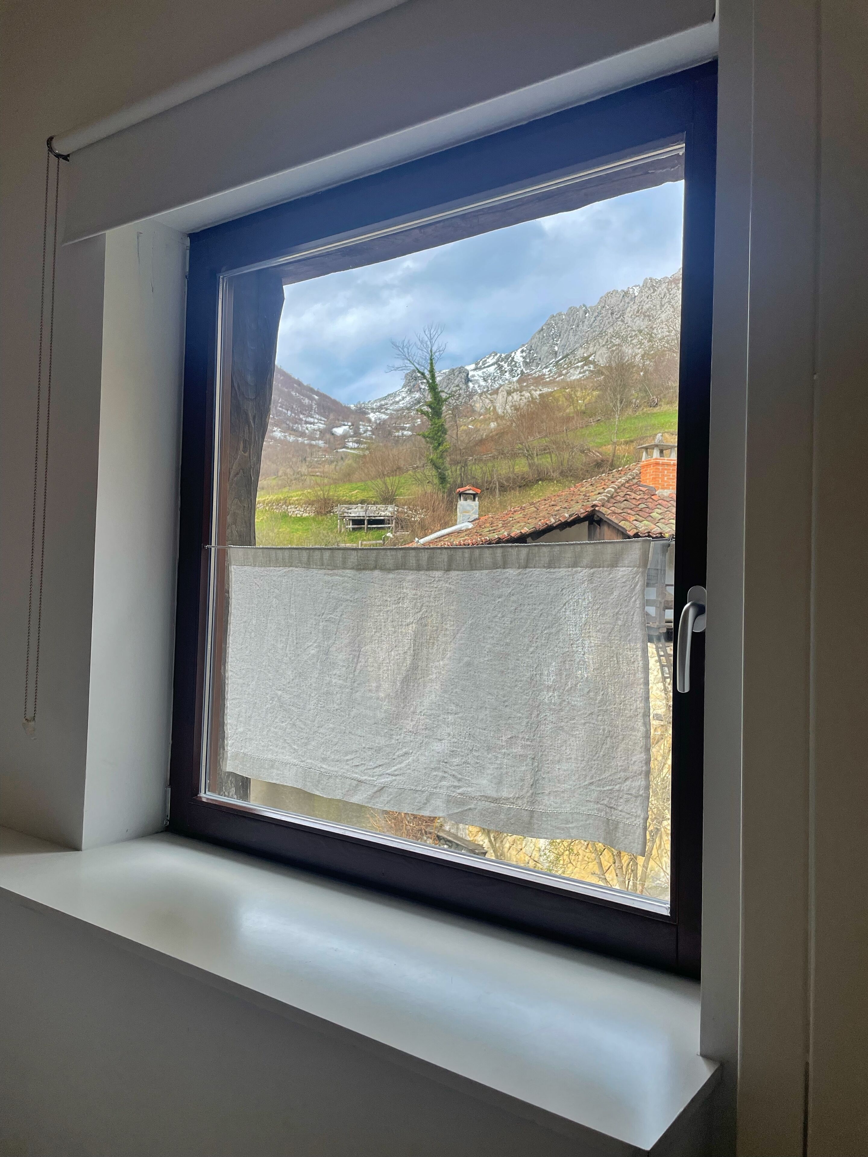 Een raam met uitzicht op een bergachtig landschap, een gebouw met een rood dak en een heldere lucht.