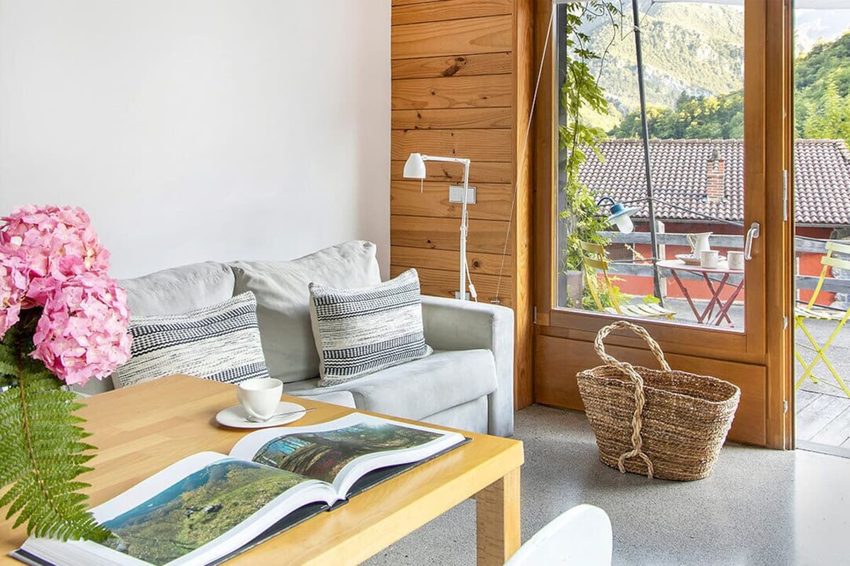 A cozy living area with a sofa, a coffee table, and a window with a view of a red-roofed building and greenery.