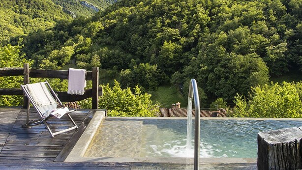 Een houten terras met een jacuzzi, lounge stoelen en een berg op de achtergrond.