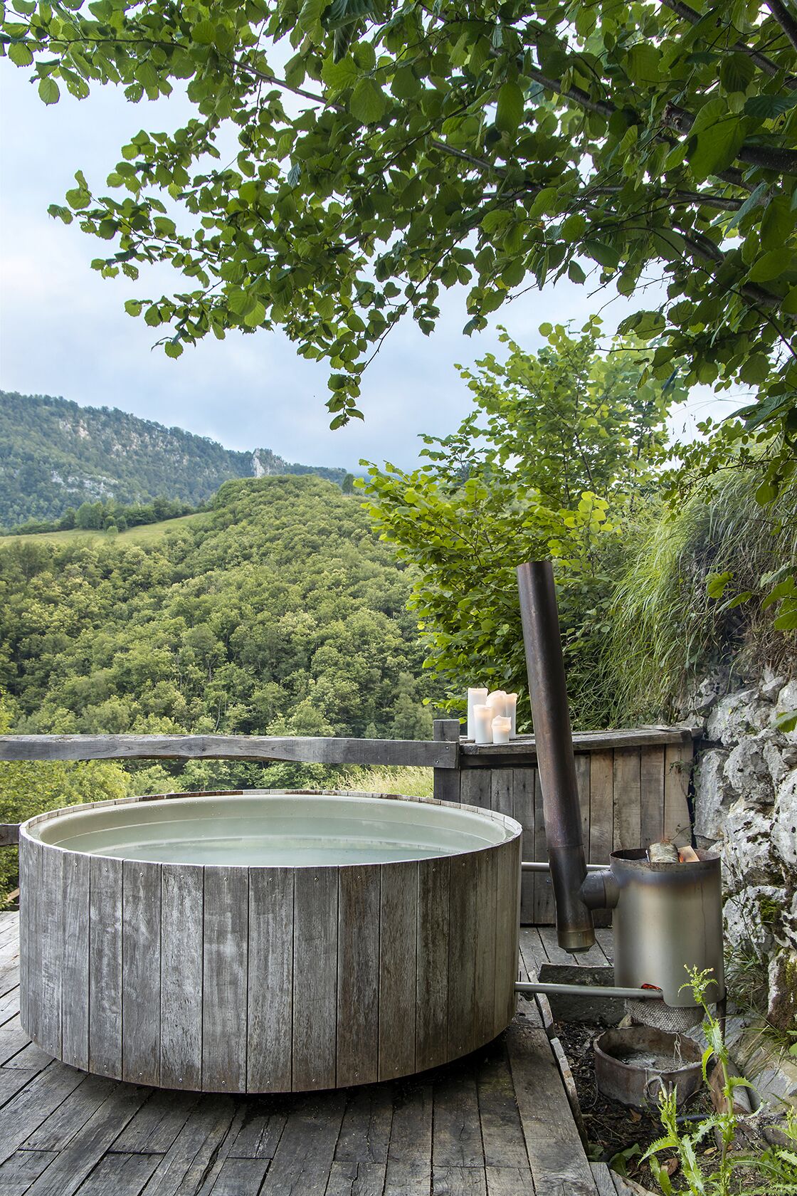 Un jacuzzi de madera con vistas a un paisaje montañoso cubierto de bosque.
