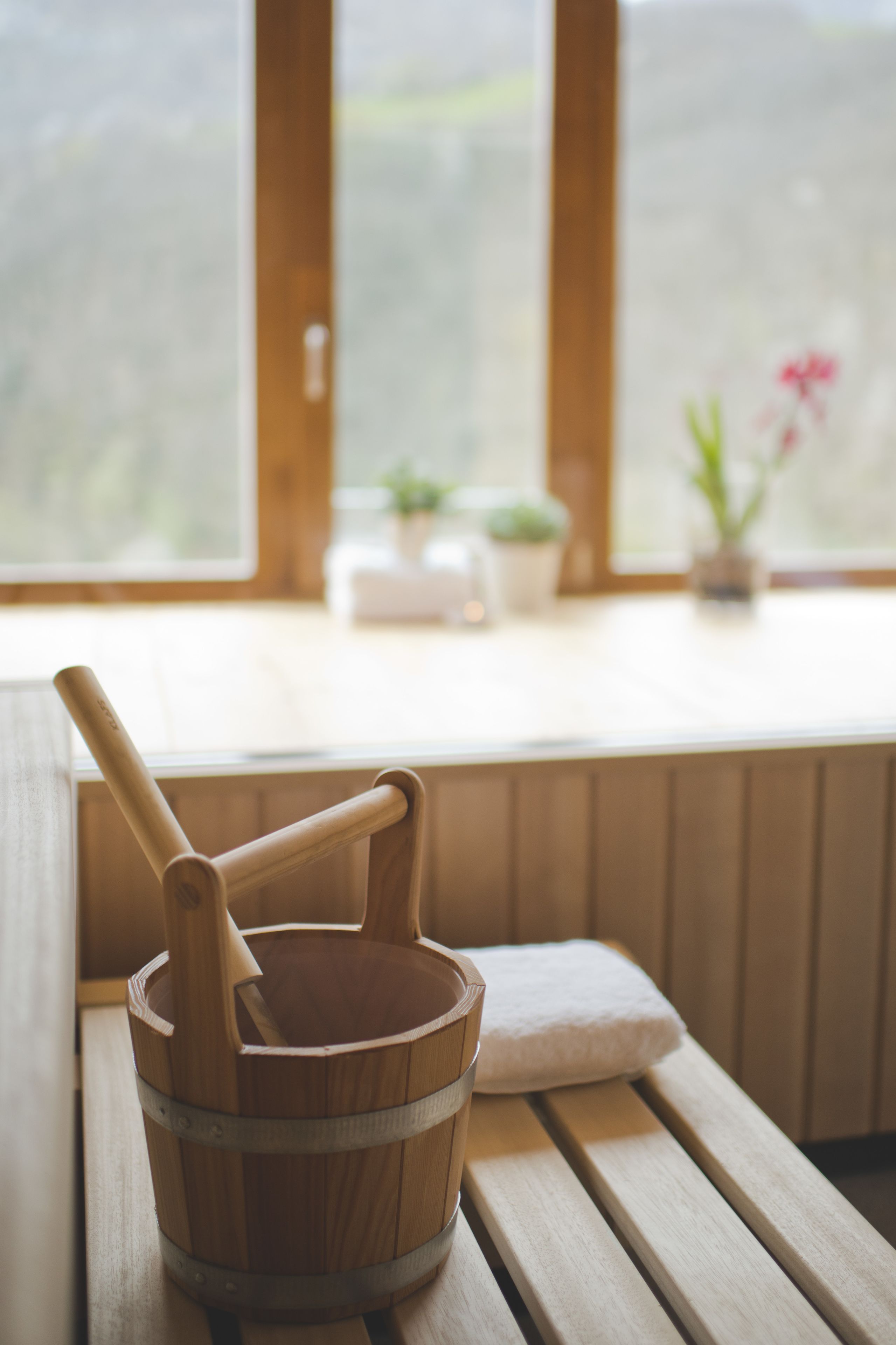 A wooden bucket with a wooden mallet on a wooden bench by a window with potted plants.