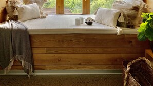Een houten chalet met een groot raam dat uitkijkt over een bebost gebergte.