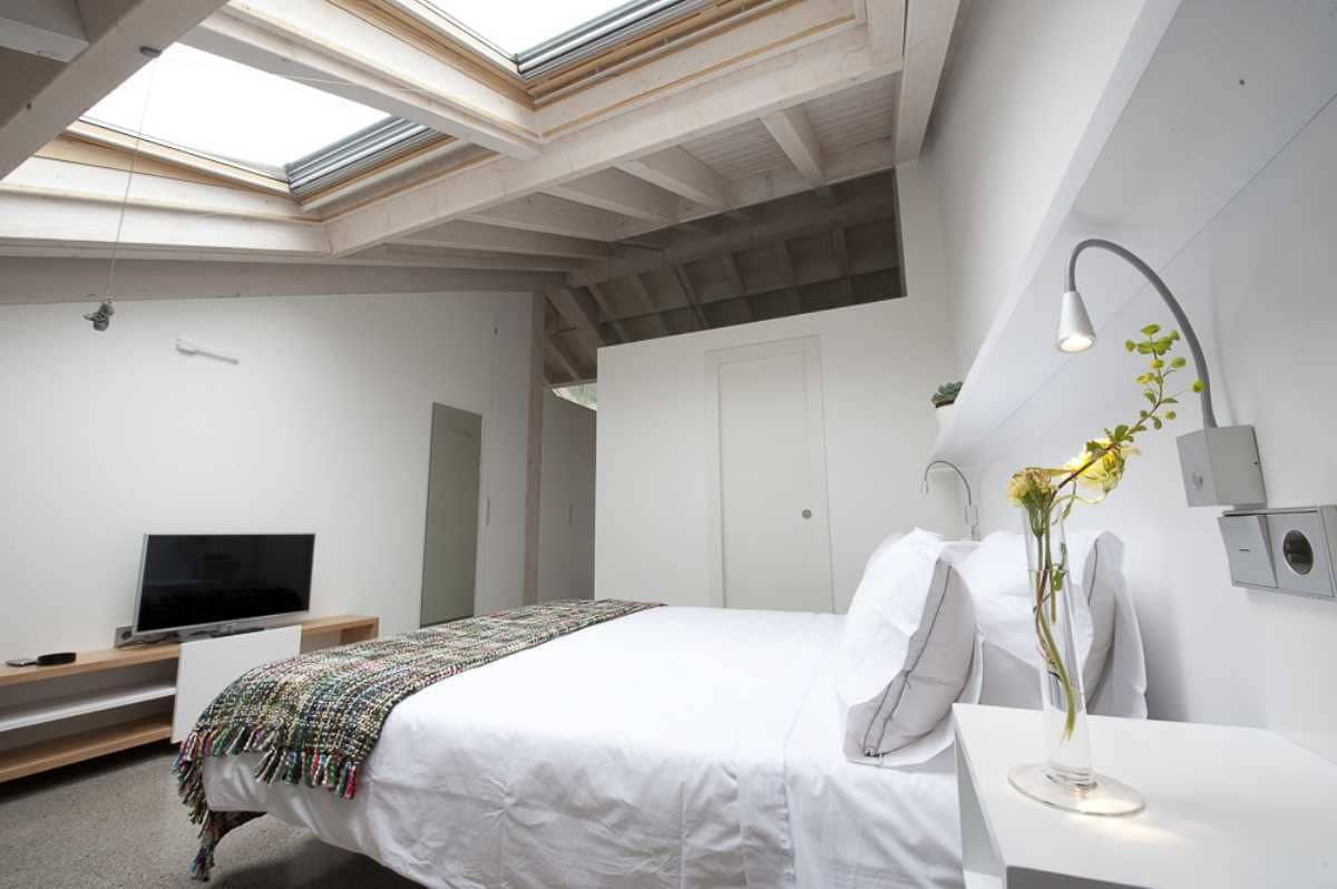 Une chambre moderne avec une lucarne, un lit, une table de chevet avec une lampe et un téléviseur.