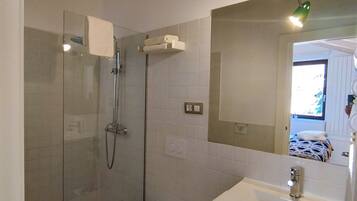 Un baño con ducha de vidrio, inodoro, lavamanos y espejo.