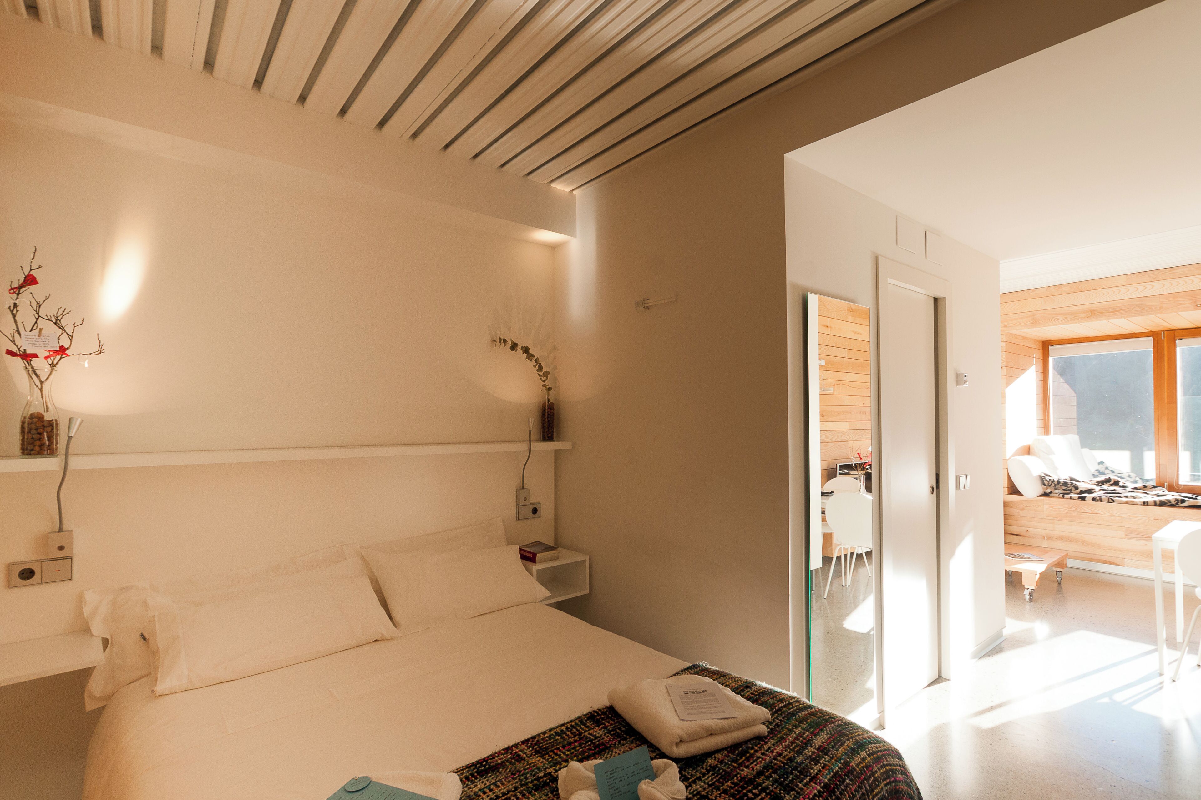 Habitación de hotel moderna con una cama grande, mesitas de noche, un escritorio pequeño y vistas al área de estar contigua.