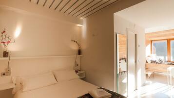 Habitación de hotel moderna con una cama grande, mesitas de noche, un escritorio pequeño y vistas al área de estar contigua.