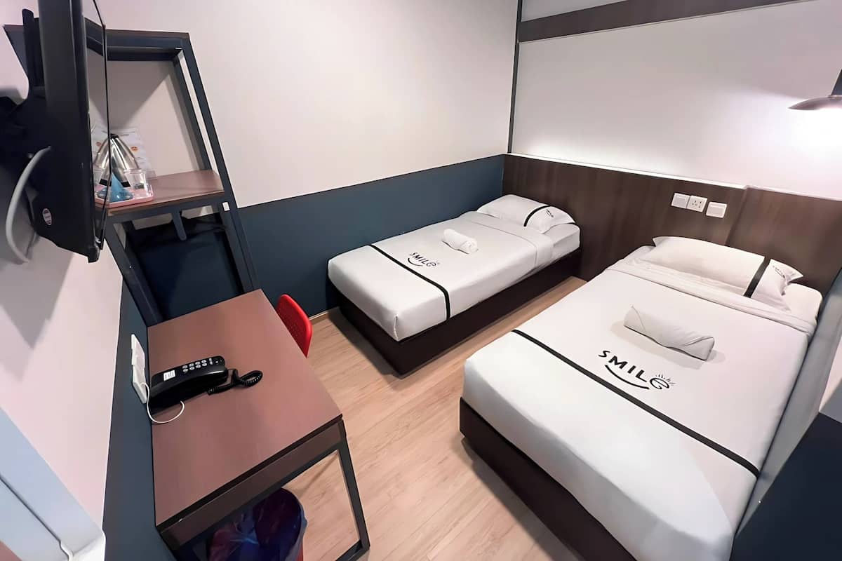 A compact hotel room with two beds, a desk, a chair, a TV, and a small table.