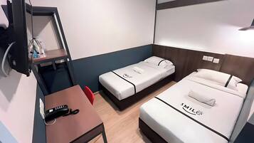 Una habitación de hotel compacta con dos camas, un escritorio, una silla, un televisor y una pequeña mesa.