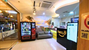 A hotel reception area with a sofa, vending machines, a computer monitor, and a wall with a 'Hotel Smile' sign. - Smile Hotel USJ (Subang Jaya)