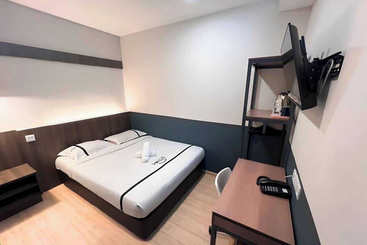 A compact hotel room with a bed, a desk, and a TV mounted on the wall.