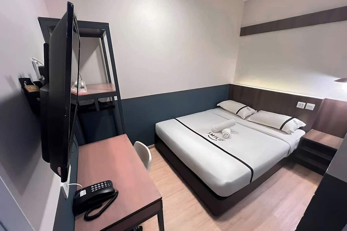 A compact hotel room with a bed, a desk with a telephone, and a TV.