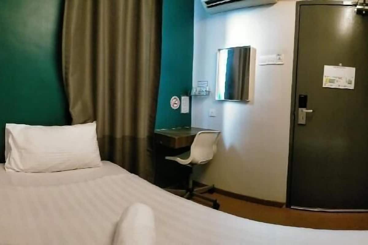 A hotel room with a bed, a desk, a chair, a door, and an air conditioning unit.