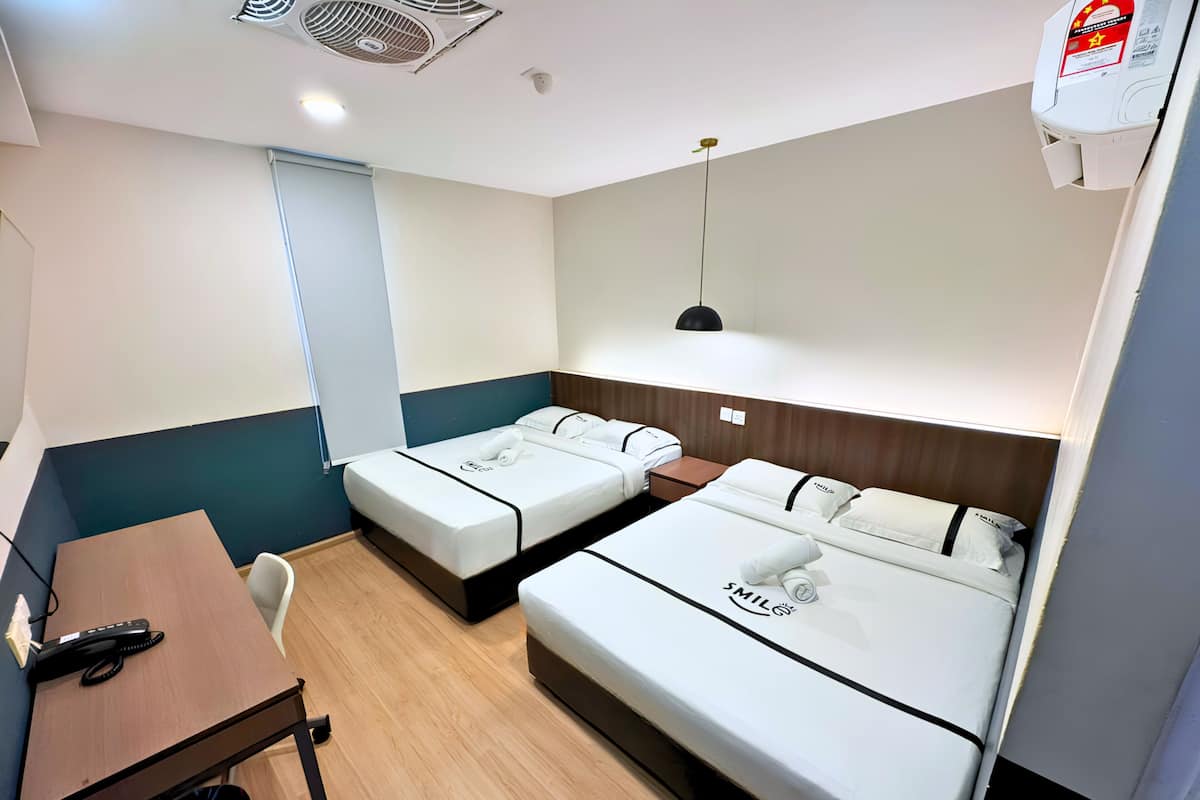 A hotel room with two beds, a desk, a chair, a desk lamp, a ceiling fan, and a wall-mounted air conditioner.