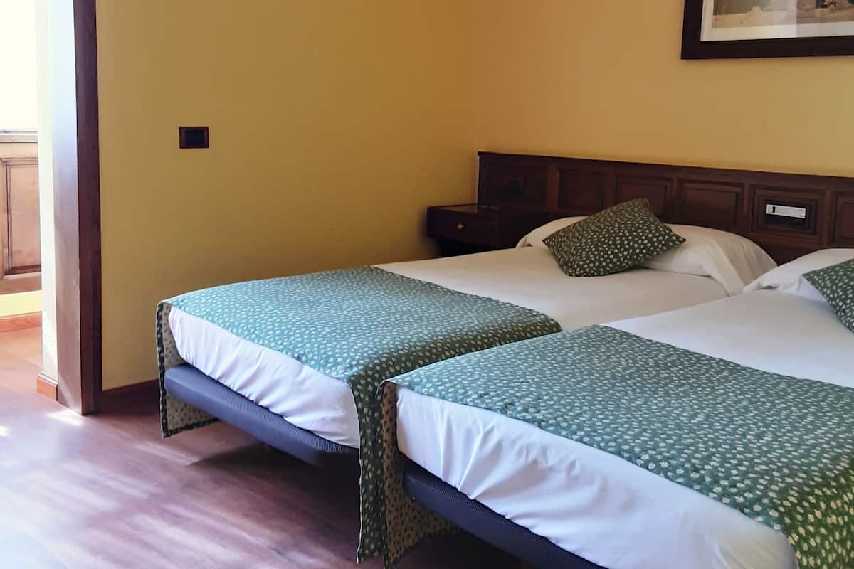 Habitación de hotel con dos camas, piso de madera, un cuadro en la pared y una mesita de noche pequeña.