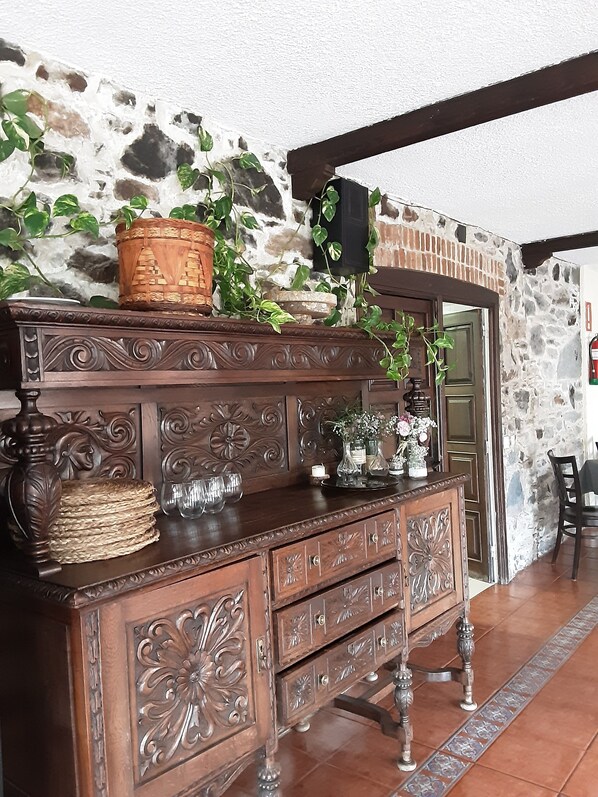 A wooden dresser with intricate carvings, a woven basket, and a potted plant against a stone wall.