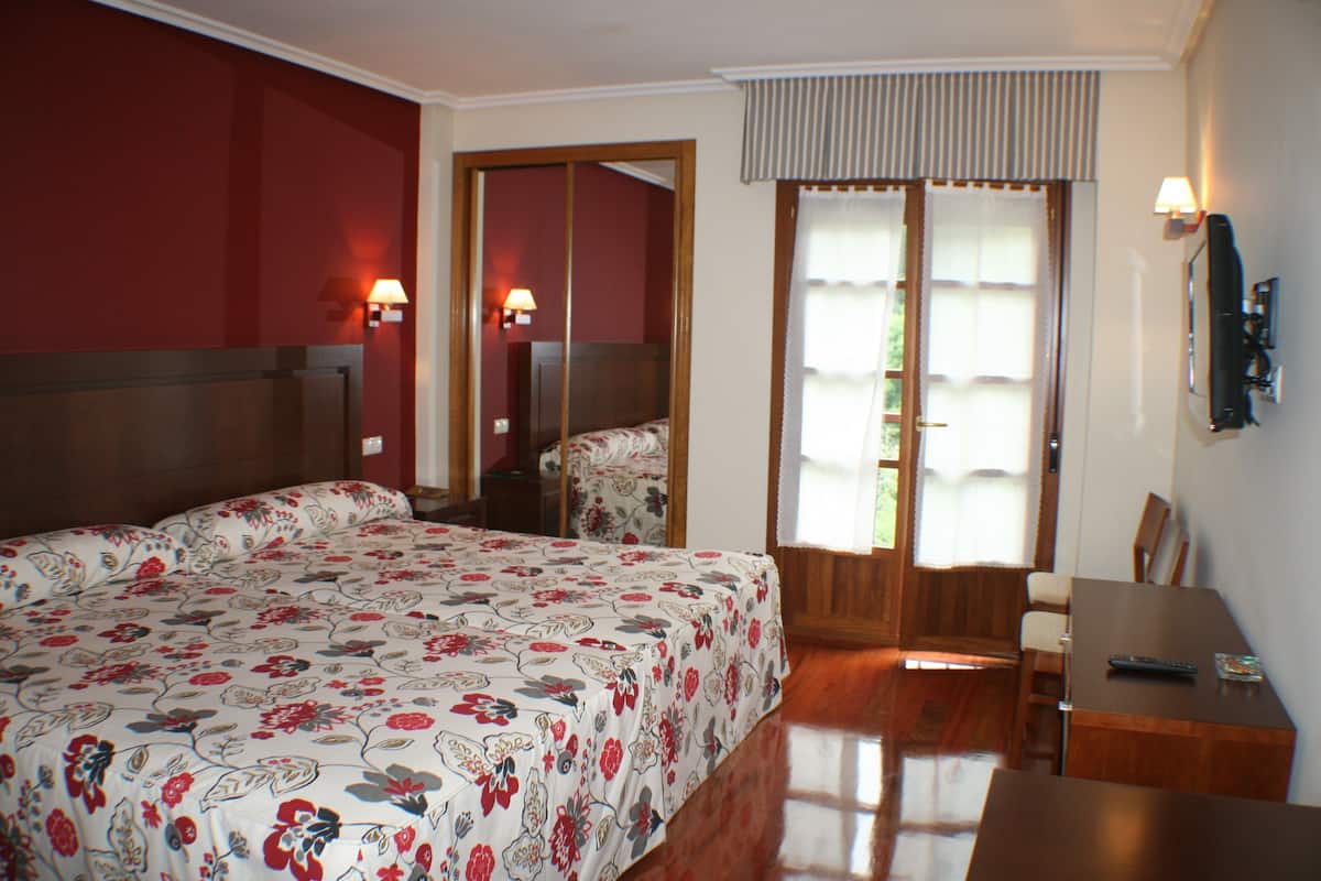 A hotel room with a large bed, a desk, and a chair. There is a mirror on the wall and a window with curtains.