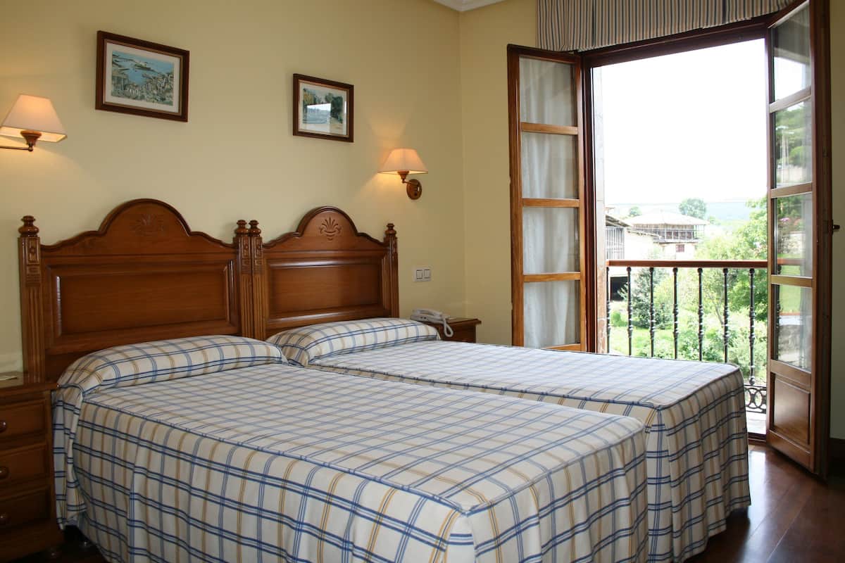 A bedroom with two beds, a wooden headboard, bedside lamps, and a balcony with a view.