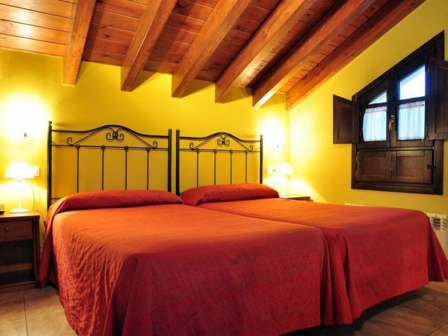 A double bed with a wooden headboard, two bedside tables with lamps, and a window with curtains.