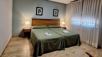 Una cama doble con ropa de cama verde, dos mesitas de noche con lámparas, un cabecero de madera y una ventana con cortinas.