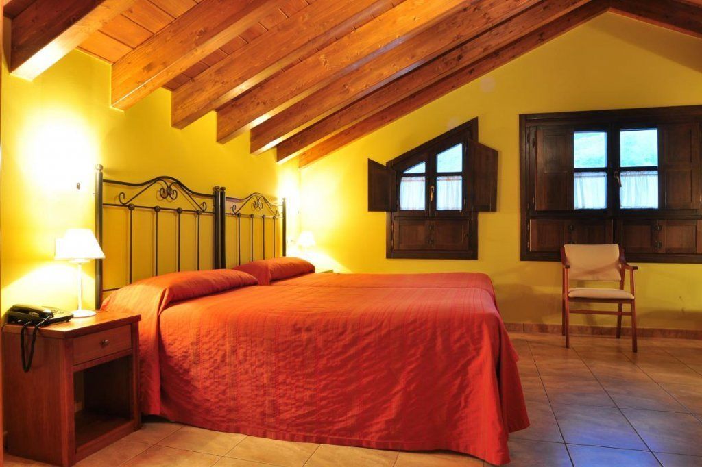 Un dormitorio con techo de madera, una cama con ropa de cama roja, una mesita de noche con una lámpara y una silla.