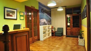 Een receptiegedeelte met een houten bureau, een boekenkast, een groene wand met een lijst en een groot raam met gordijnen.