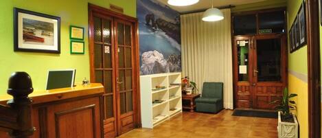 A reception area with a wooden desk, a bookshelf, a green wall with a framed picture, and a large window with curtains.
