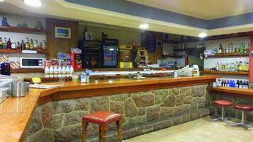 Zona de bar con mostrador de piedra, taburetes de madera y estanterías llenas de botellas.