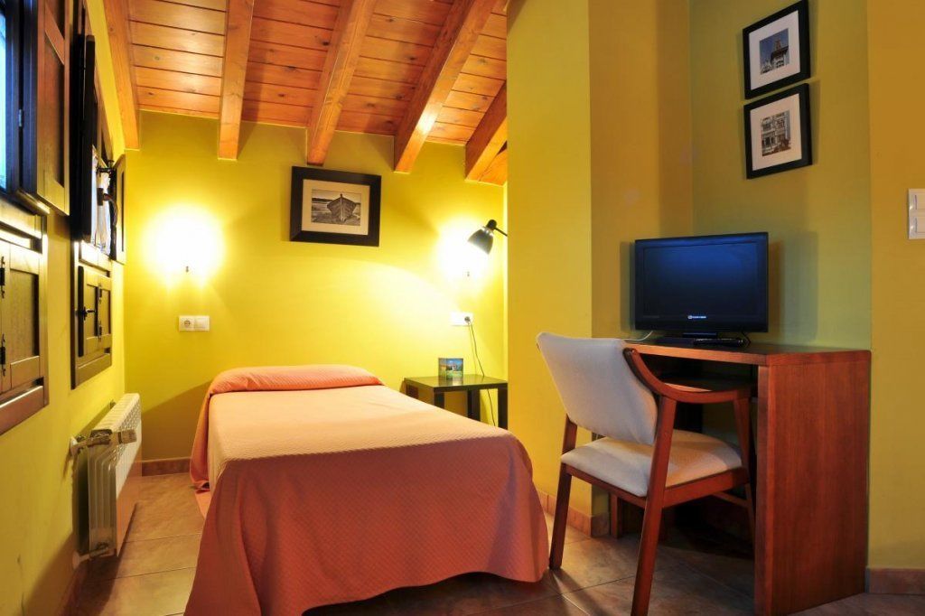 Quarto de hotel com duas camas, uma escrivaninha com cadeira, televisão e quadros nas paredes.