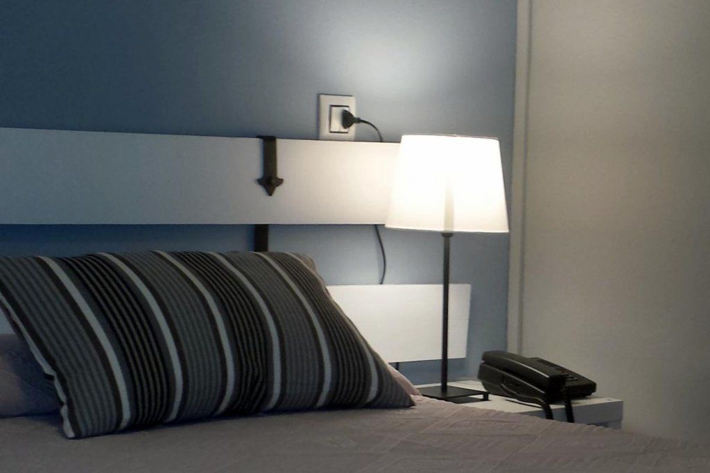 A bed with a striped pillow, a bedside lamp, and a phone on a nightstand.