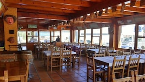 Een restaurant met houten tafels en stoelen, grote ramen en een betegelde vloer.