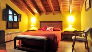 Een slaapkamer met een houten plafond, twee bedlampen, een bed met rode beddengoed, een nachtkastje, een stoel en een raam met gordijnen.