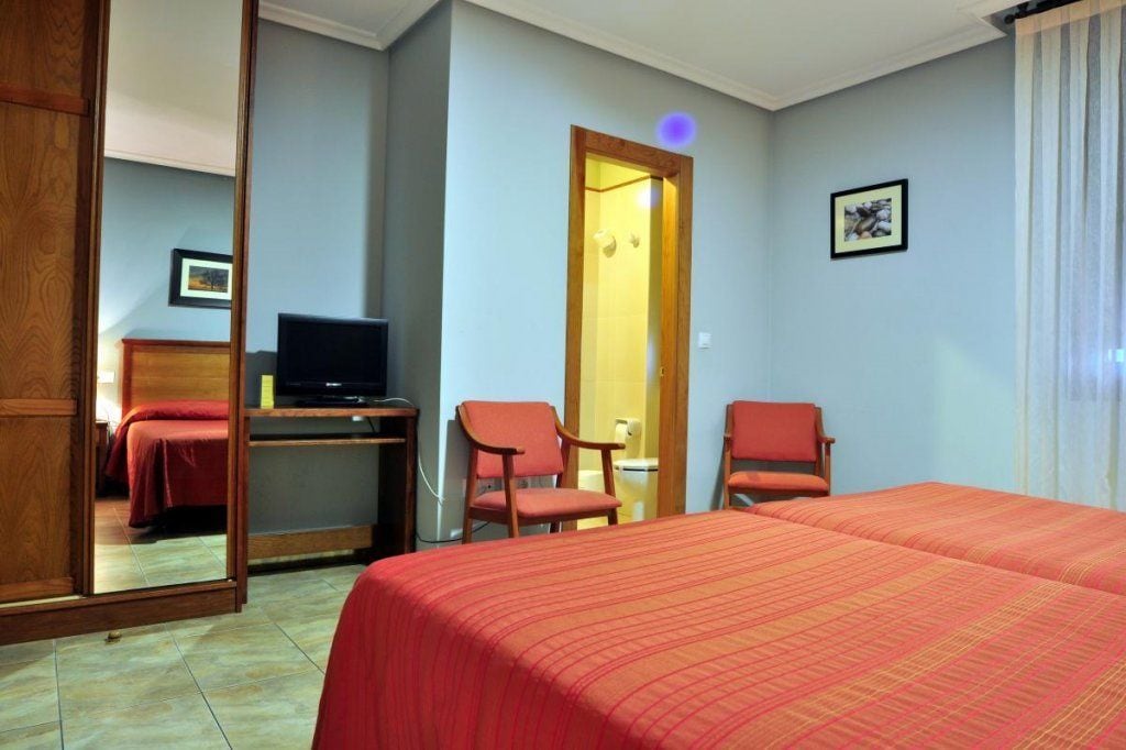 A hotel room with a bed, two chairs, a desk with a television, and a door leading to another room.