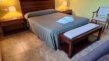Habitación de hotel ordenada con cama, mesitas de noche, una silla y un banco.