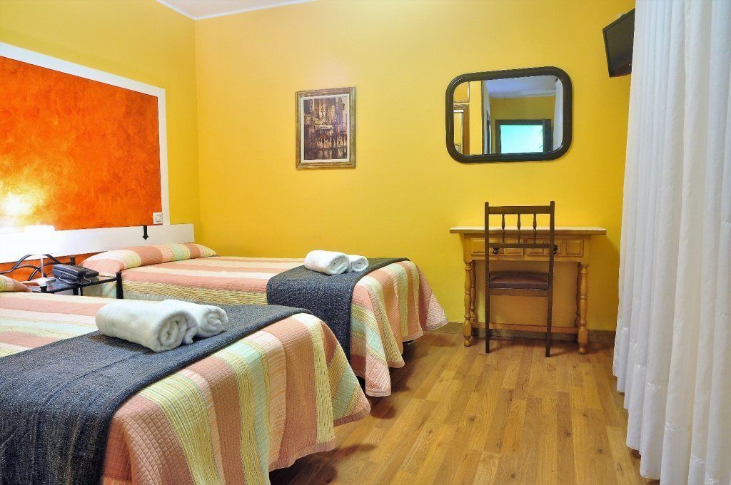 A hotel room with two beds, a desk, a chair, a mirror, and a picture on the wall.