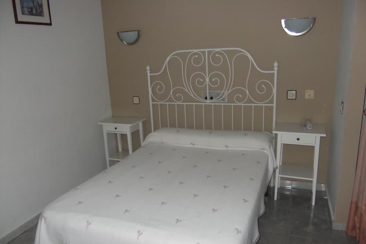 Un dormitorio con una cama, dos mesitas de noche y lámparas de pared.