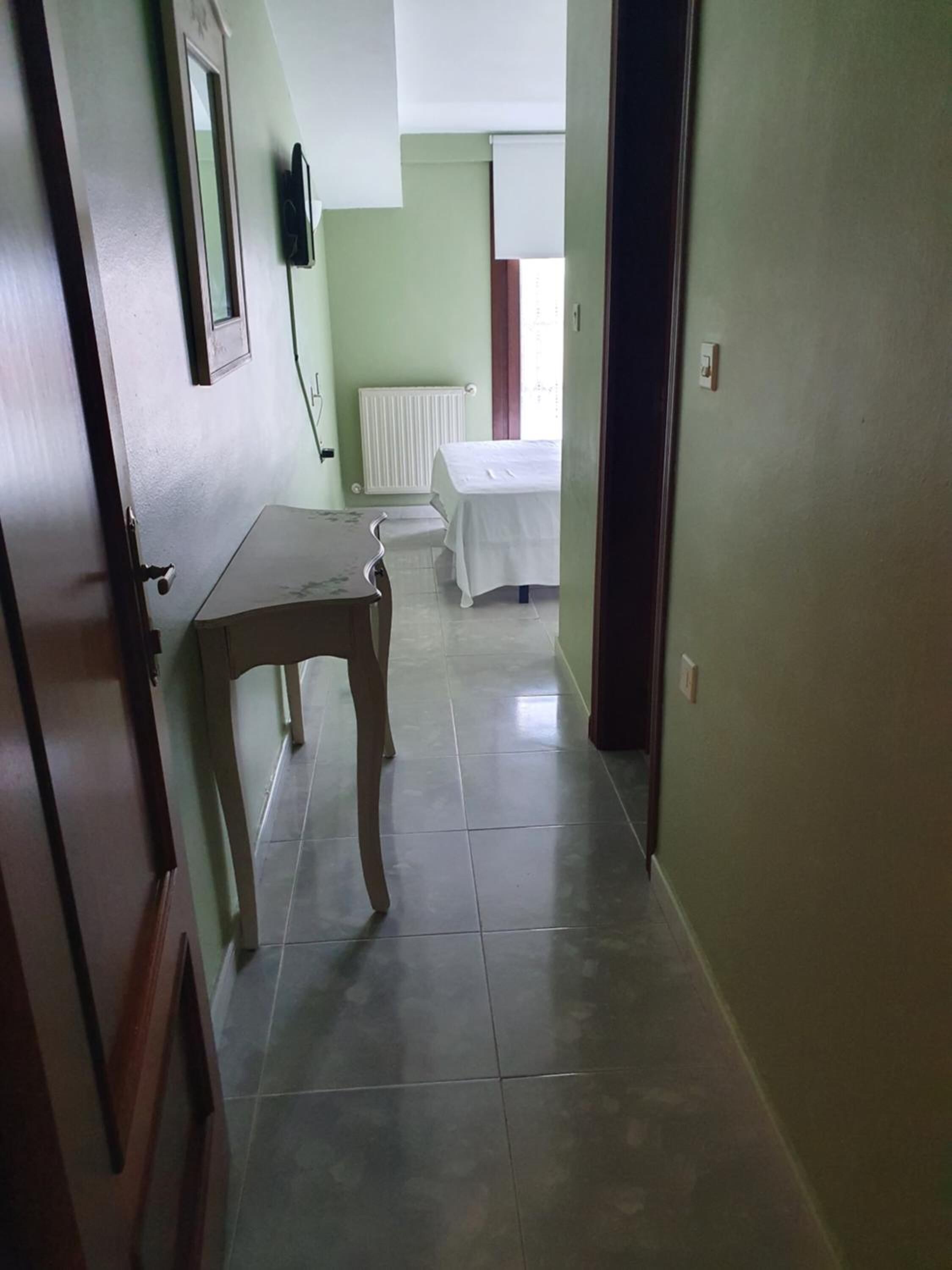 A hallway with a wooden table and a bed in the background.