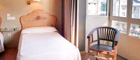 A hotel room with a bed, a chair, a lamp, and a window with a view of buildings.