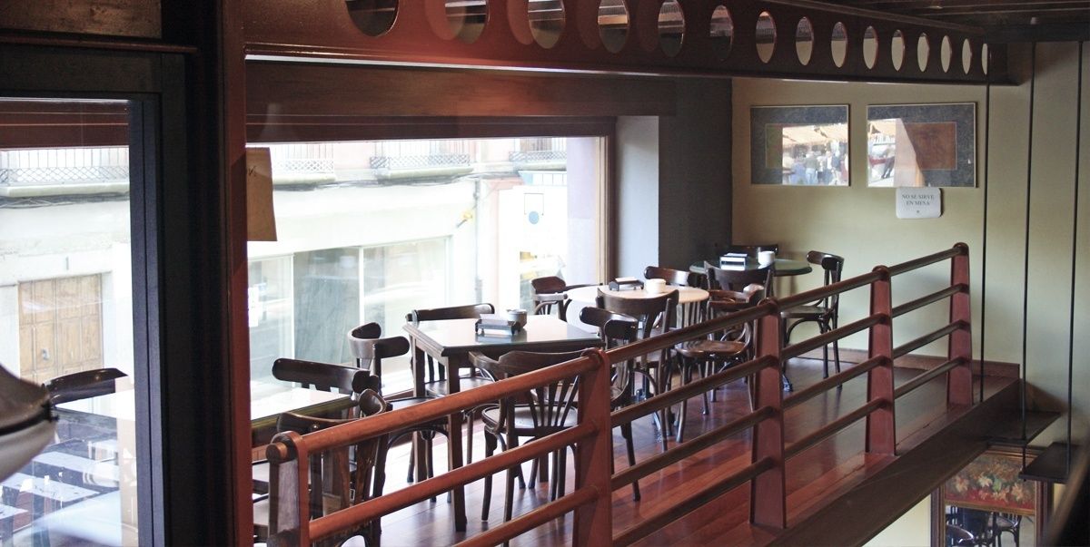 A restaurant with wooden tables and chairs, a wooden railing, and a view of the street outside.