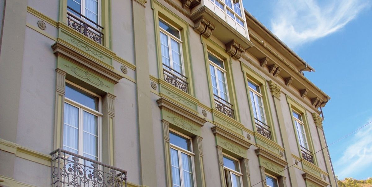 En byggnad med flera våningar, utsmyckad med detaljerad arkitektur, inklusive dekorativa lister och en balkong med smidesjärnsräcken.