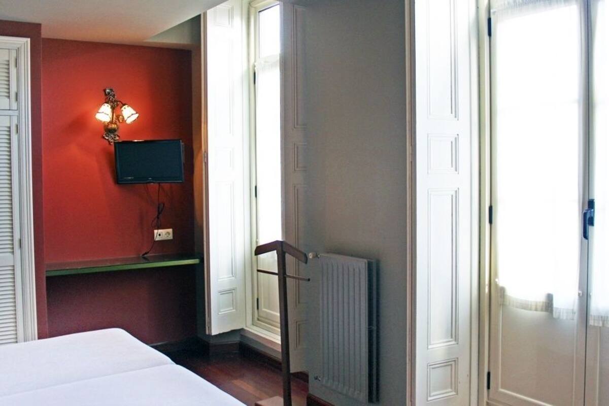 A bedroom with a bed, a television, a radiator, and a door with a window.