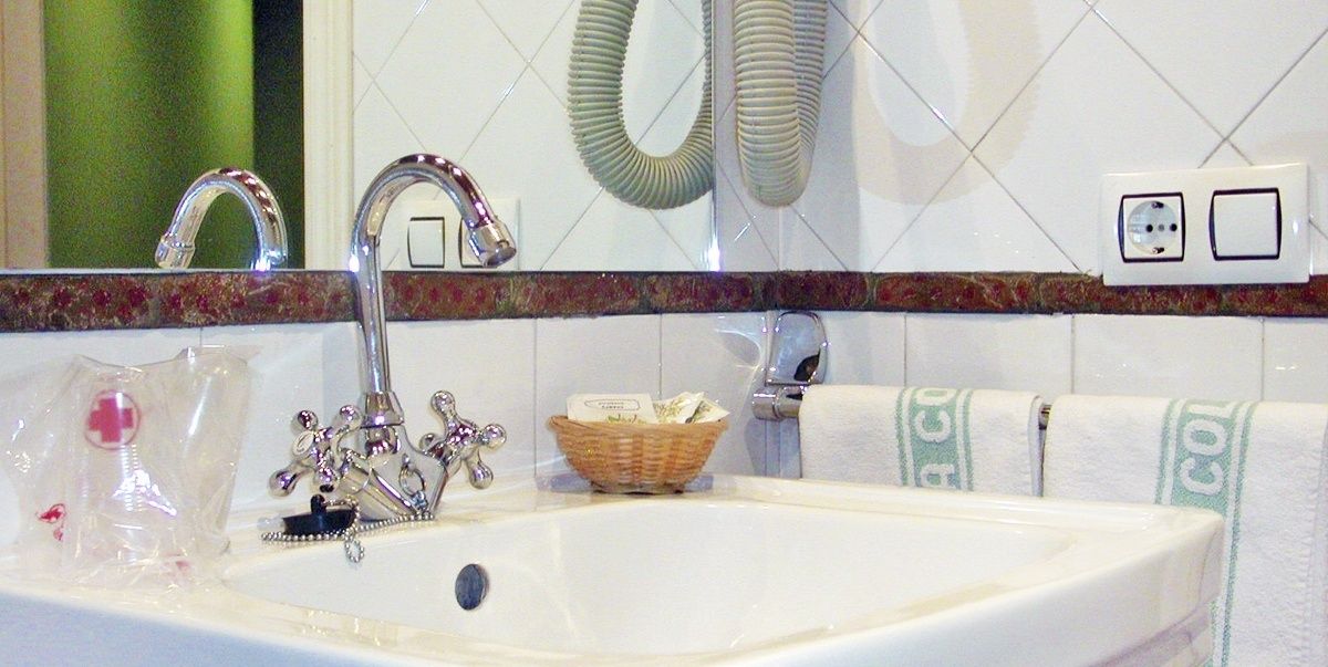 A bathroom with a white sink, chrome faucet, and a mirror above it. There is a green towel hanging on the wall and a basket with toiletries on the sink.