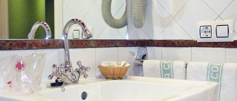 A bathroom with a white sink, chrome faucet, and a mirror above it. There is a green towel hanging on the wall and a basket with toiletries on the sink.