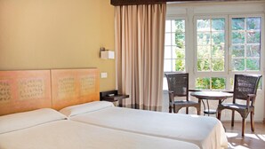 A hotel room with two beds, a small table, and chairs near a window with a view of greenery. - La Colmena (Valdes)