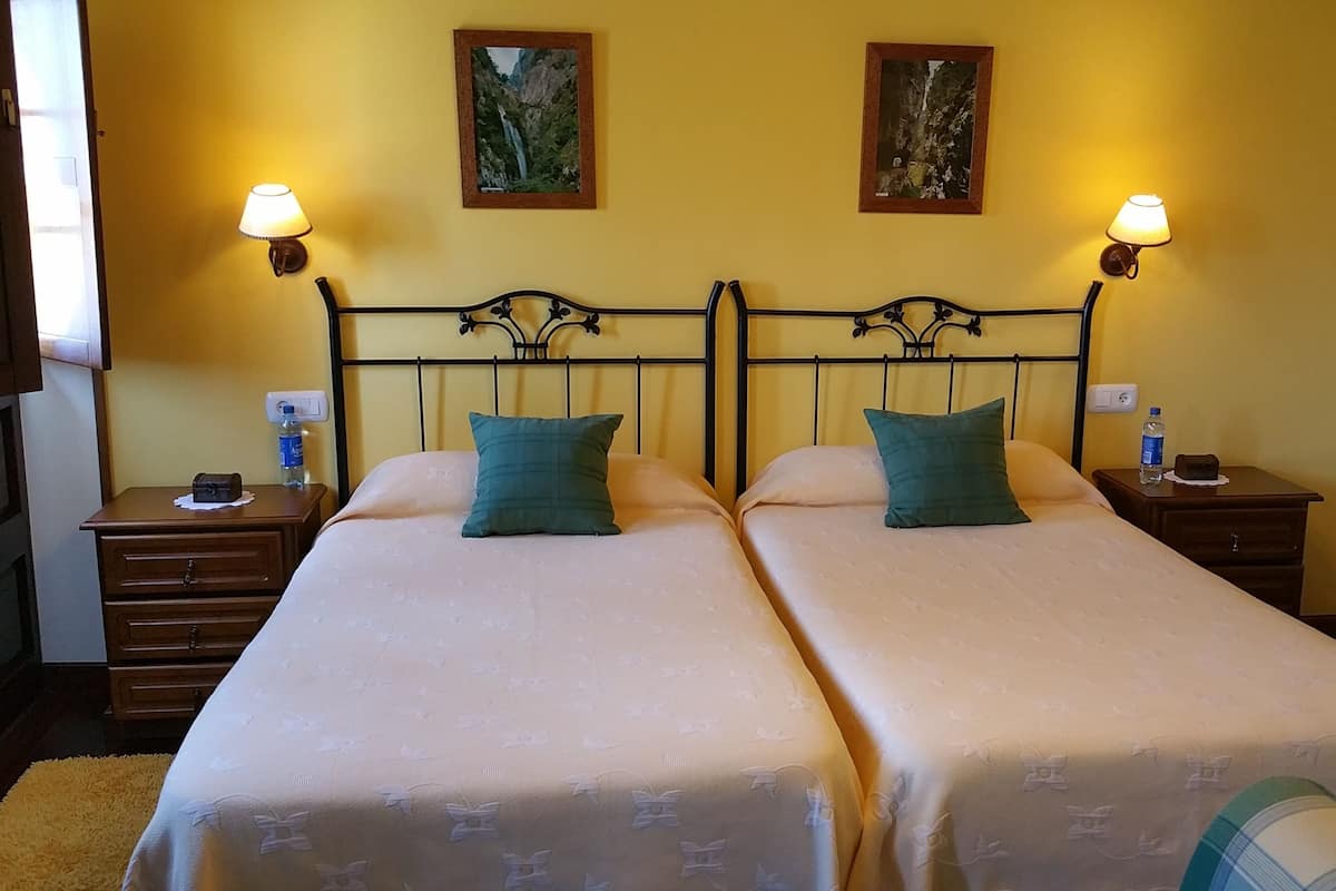 A double bed with a headboard, two bedside tables, two wall-mounted lamps, and two framed pictures on the wall.